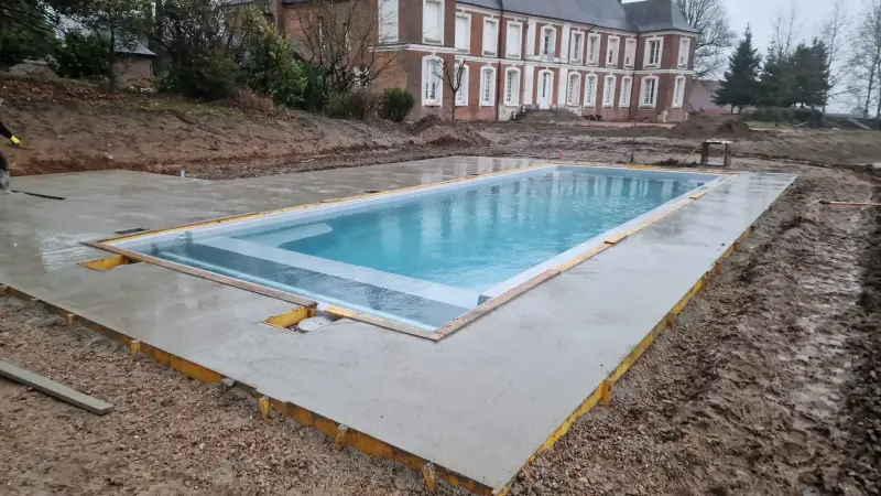 Terrassement de piscine avec dalle béton devant une demeure en briques, Eure